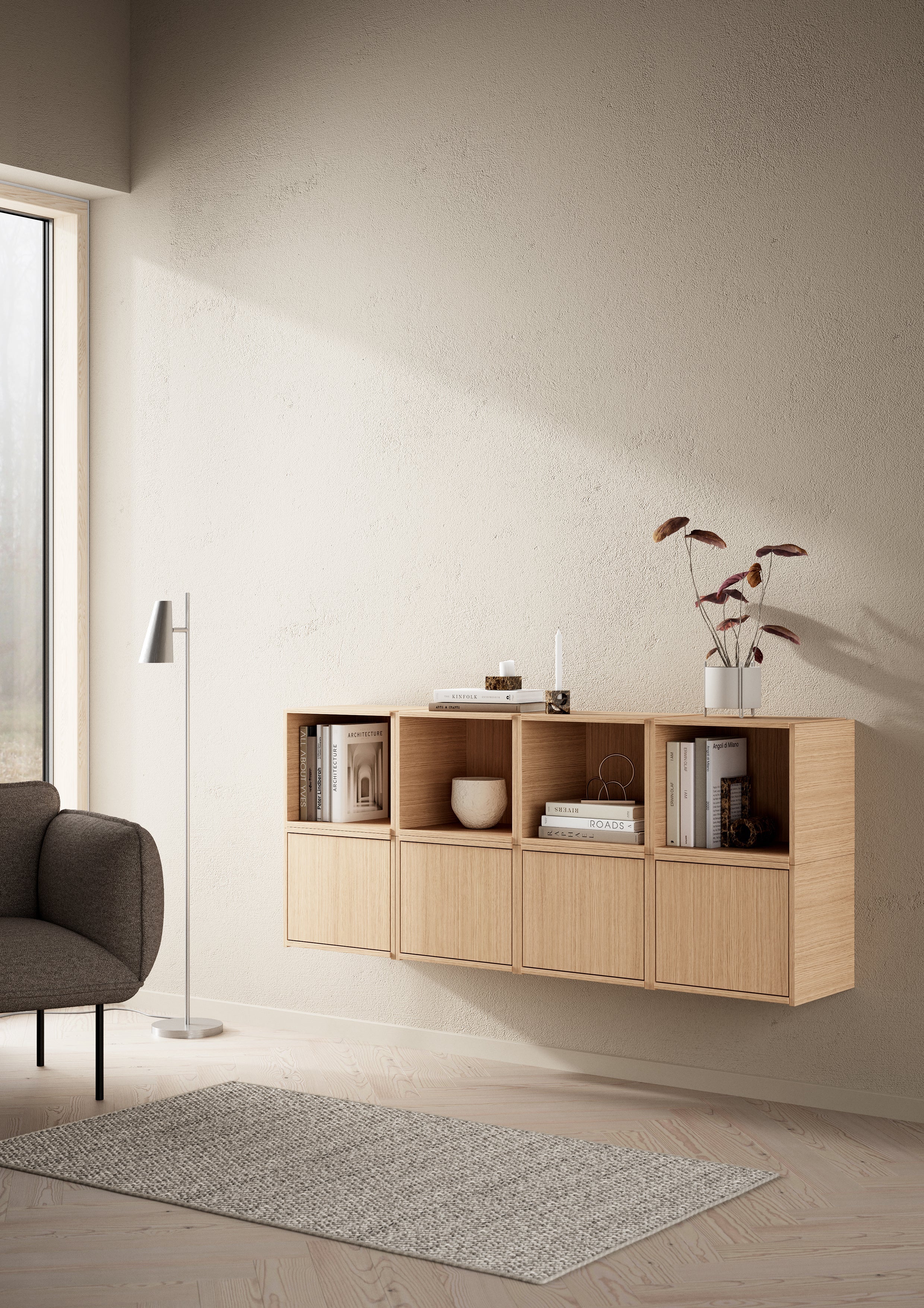 Væghængt modulært opbevaringssystem i egetræ dekoreret med bøger, foran tæppe belyst af sollys gennem vindue.