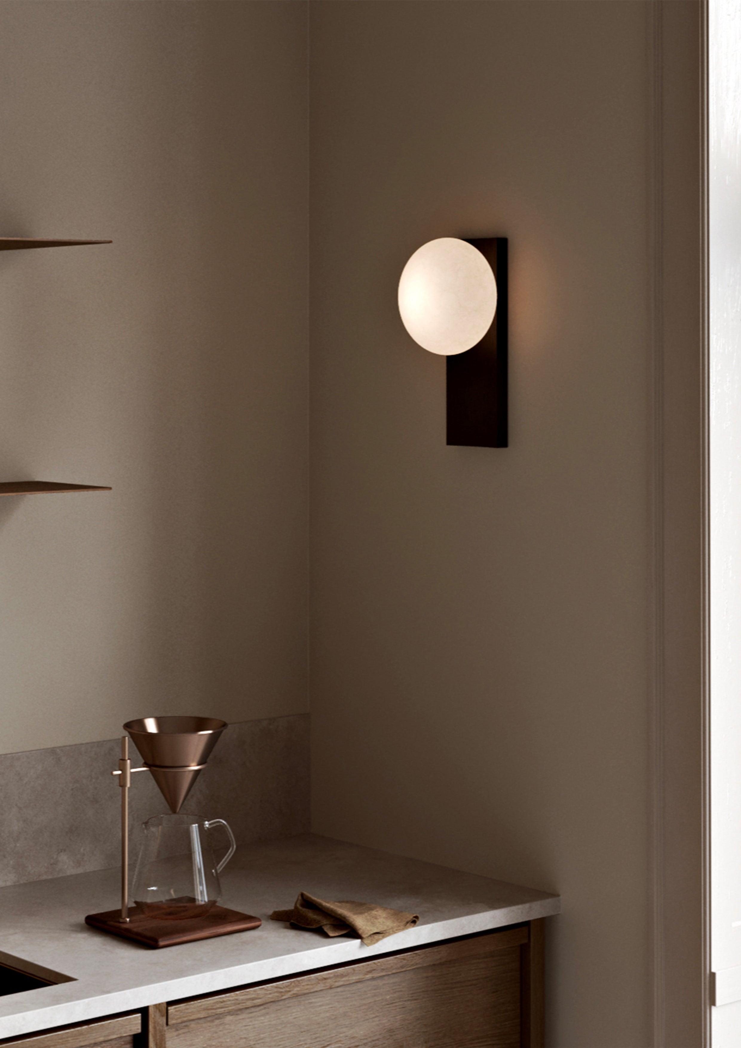 Væglampe i sortmalet ask med rund opalglaskuppel over køkkenbord.