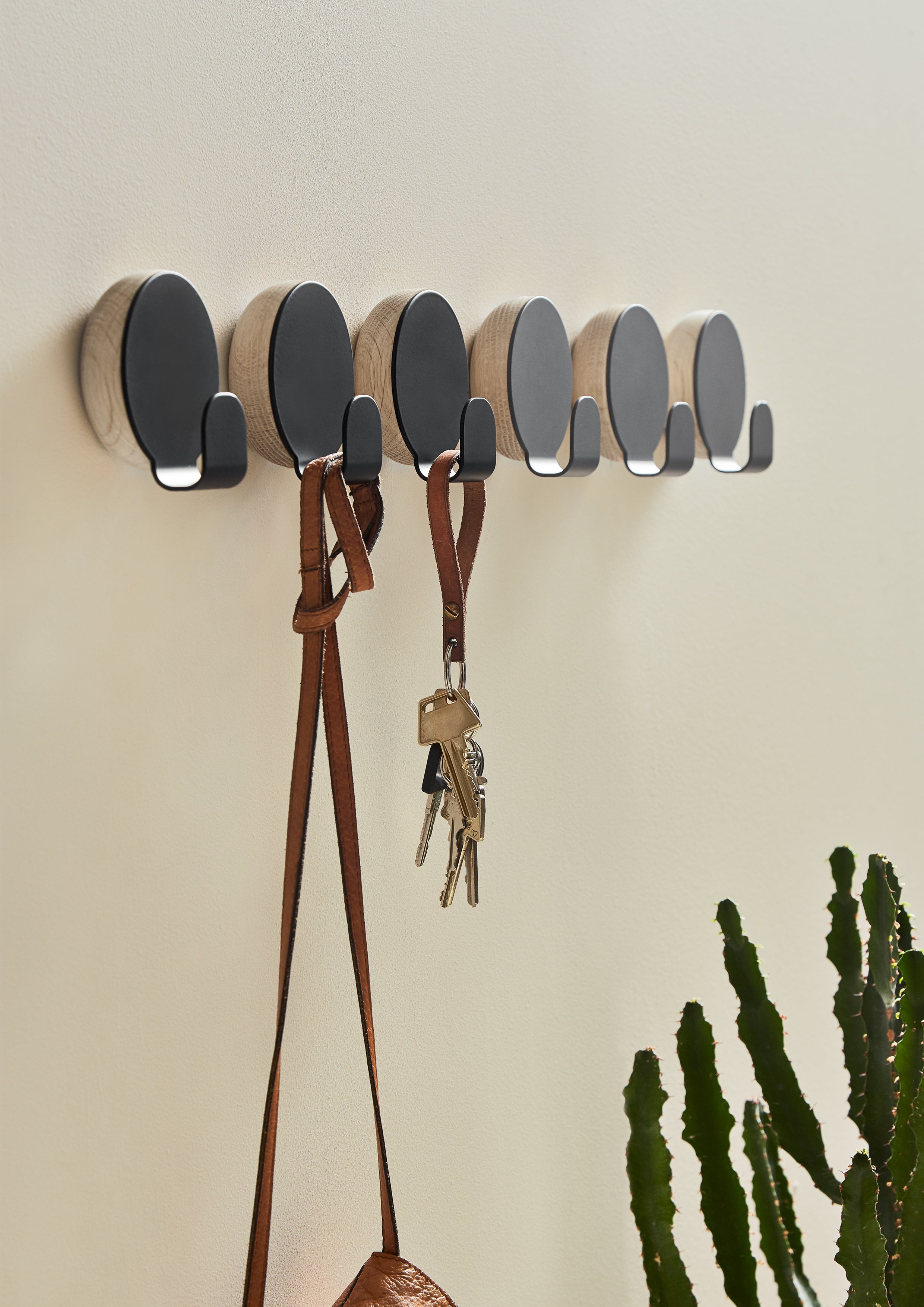 Runde knager i egetræ og metal hængende på række, en med nøglesnor, en med taske.