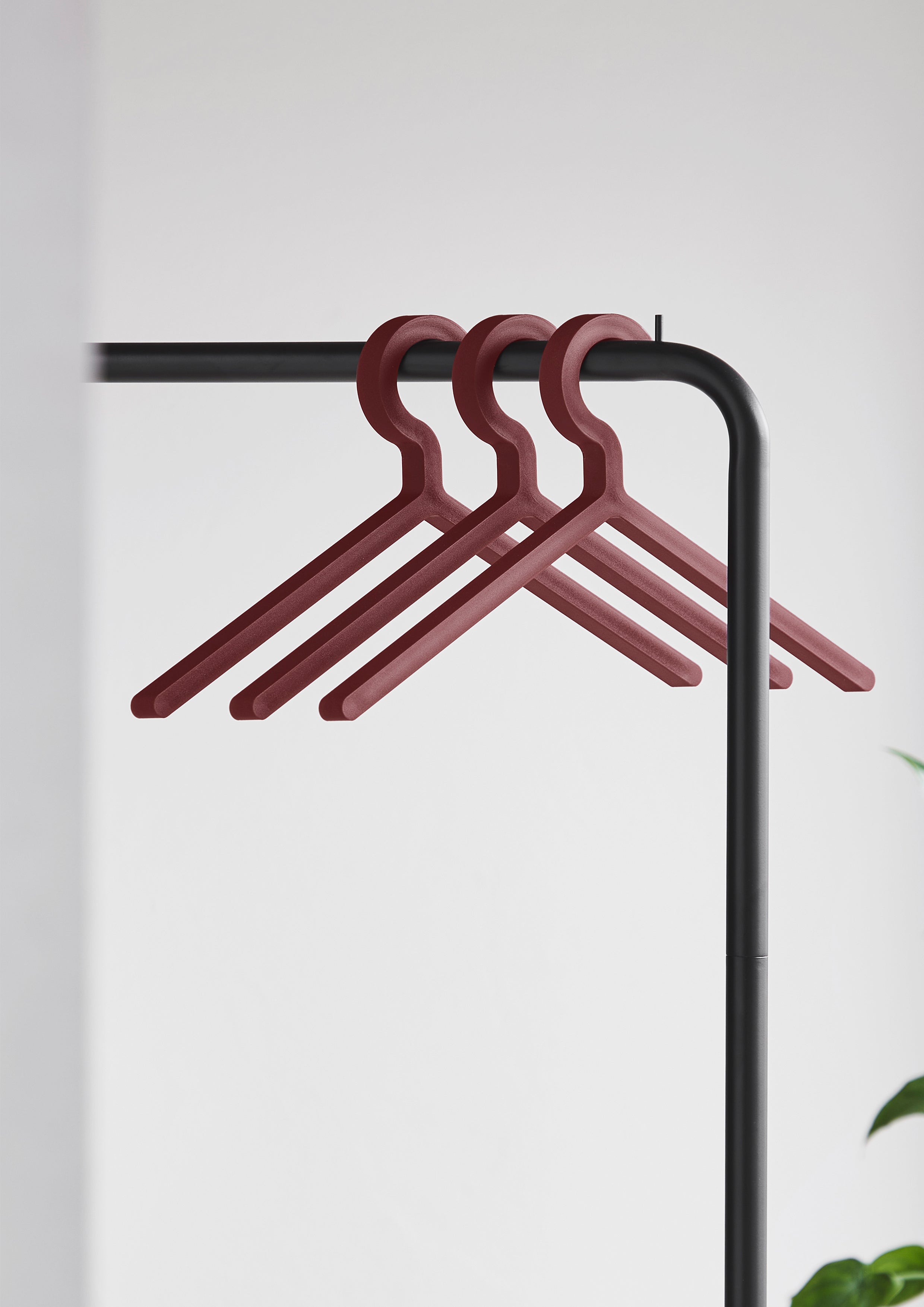 Tre bøjler i dyb rød hængende på sort tøjstativ.