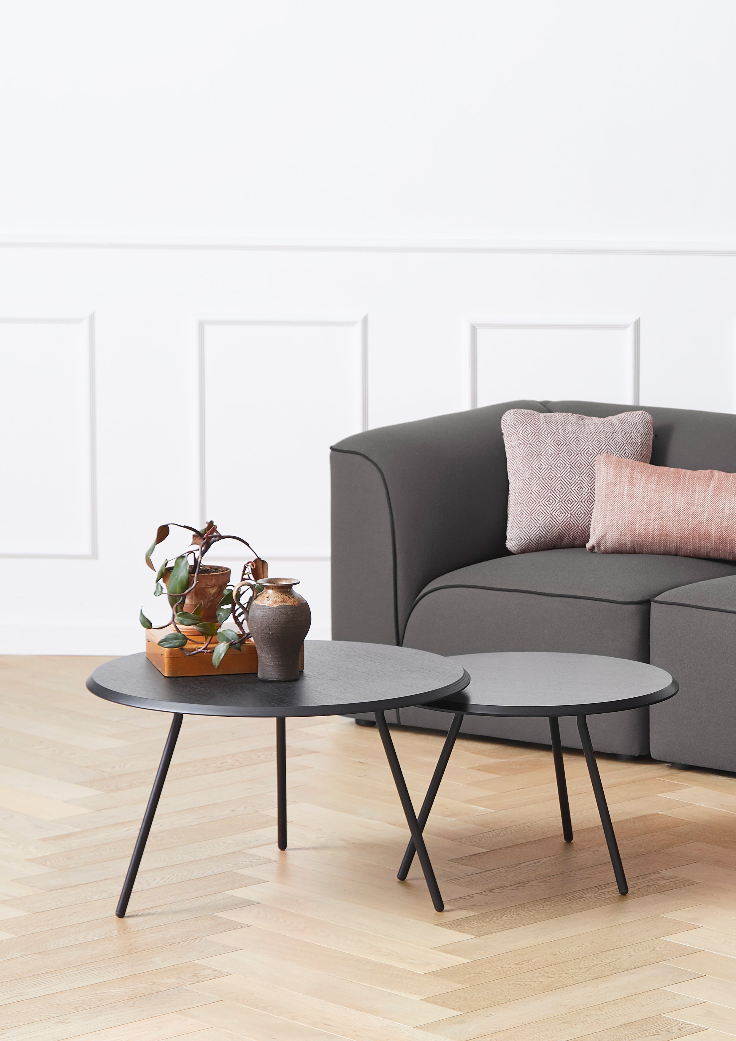 To runde minimalistiske sofaborde i sortmalet ask med sorte metalben i forskellige højder foran sofa.