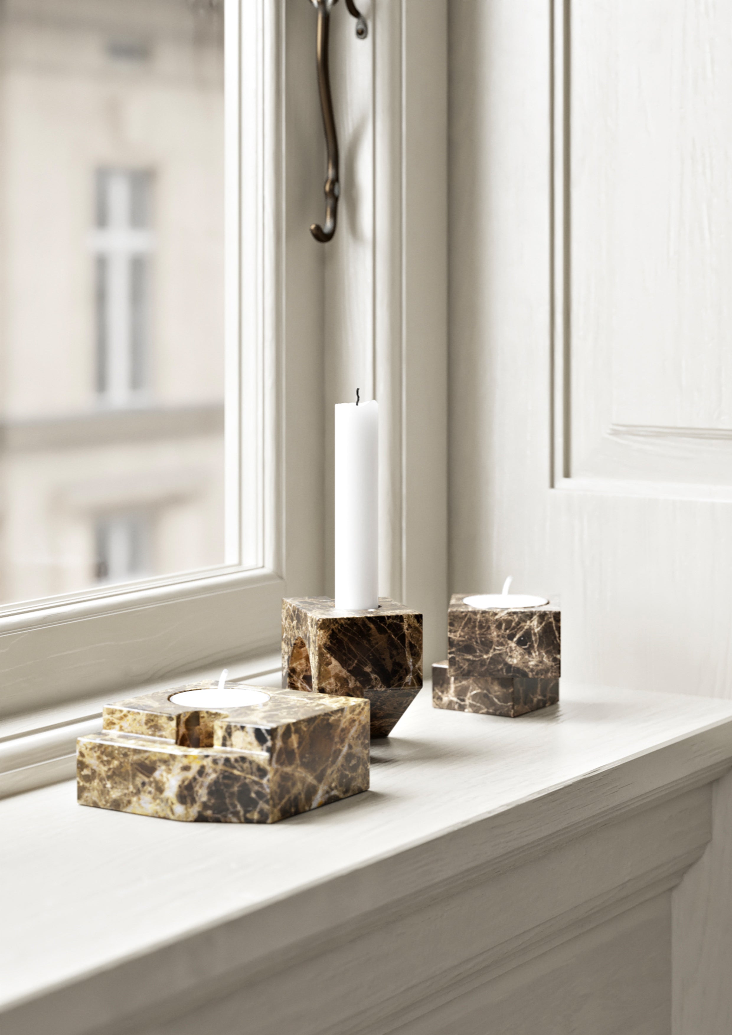 Tre små lysestager i brun massiv marmor på vindueskarm.